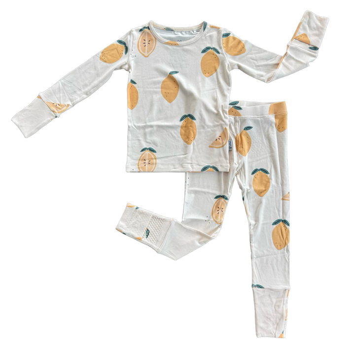 A two-piece children's pajama set featuring a long-sleeve top and matching pants, both in white with a repeating lemon print, laid flat on a white background.