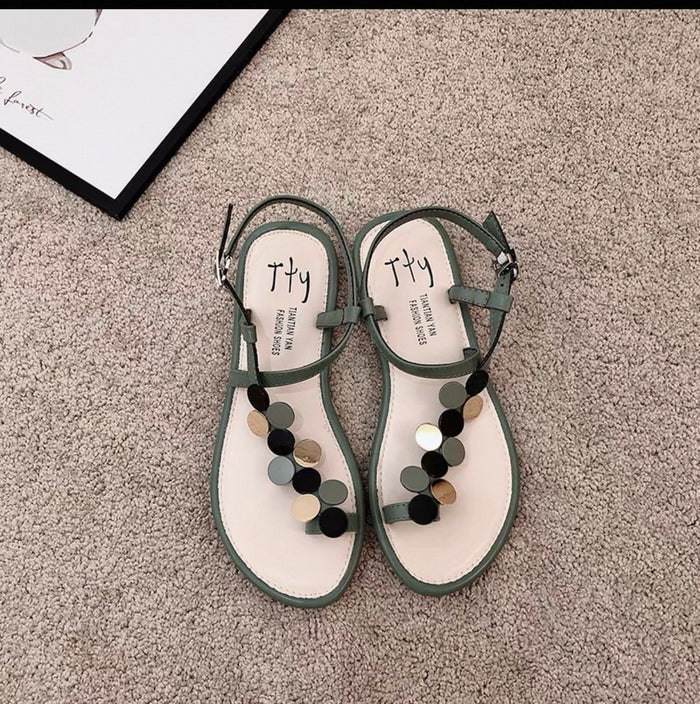 Pair of green sandals with pom-pom details on a carpeted floor.
