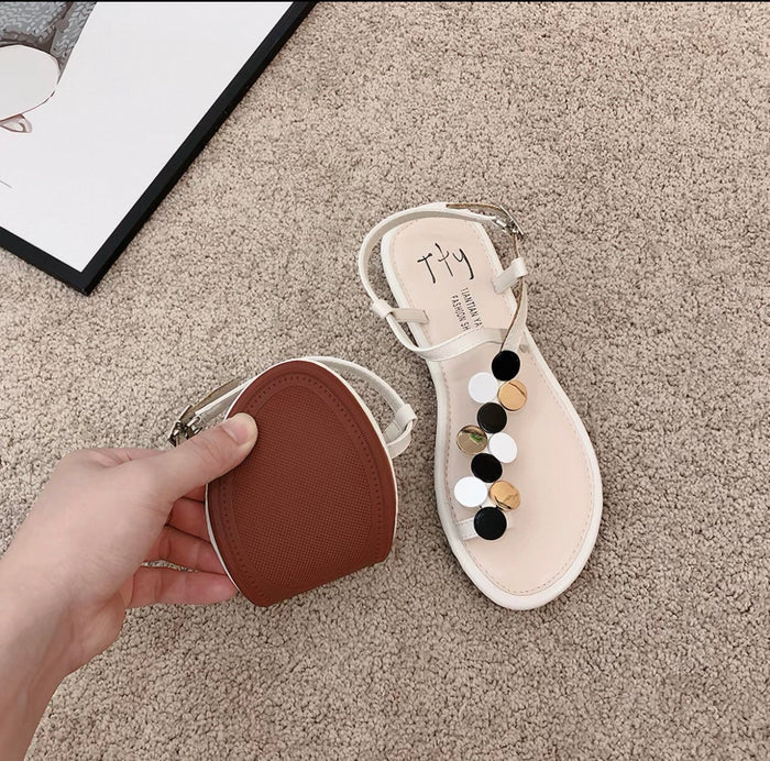 Beige sandal with decorative elements on a beige carpet, held by a hand.