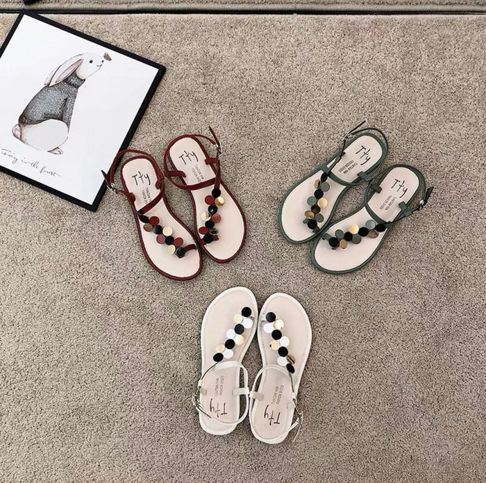 Pair of white sandals with colorful pom-poms on a gray surface next to a framed picture.