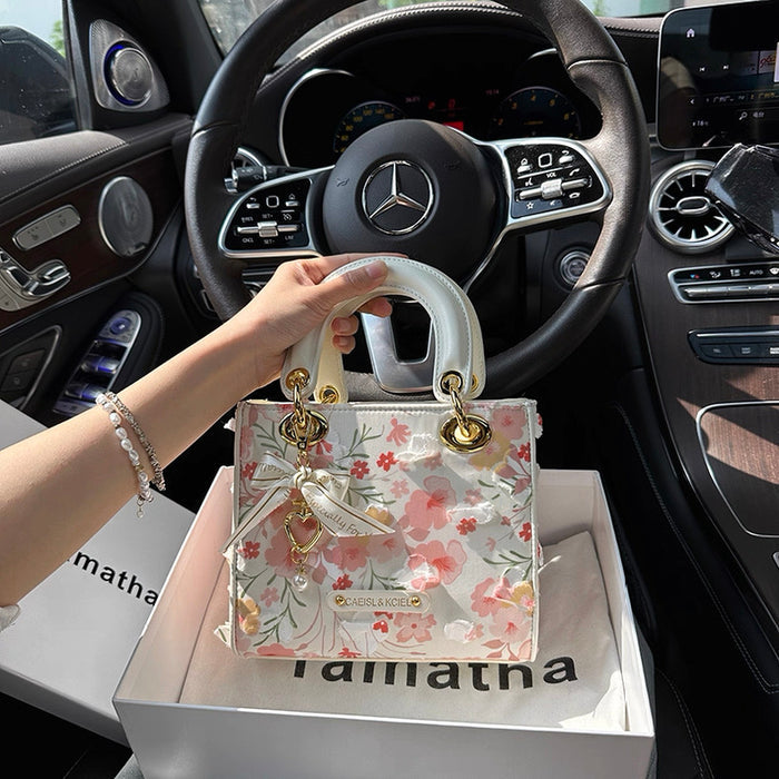 Floral handbag held by a hand in front of a car interior with a visible Mercedes logo.