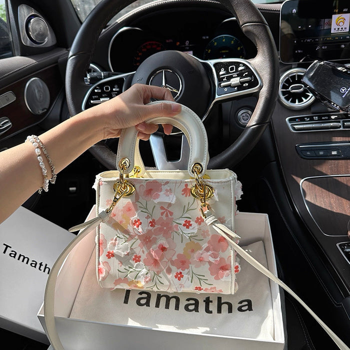 Hand holding a floral handbag with 'Tamatha' branding inside a car.