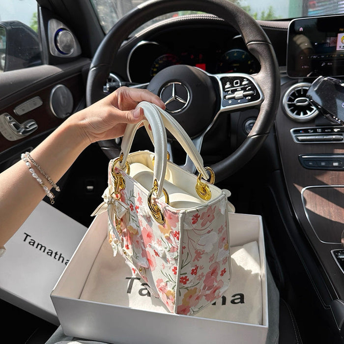 Floral handbag in a box held by a hand inside a car.