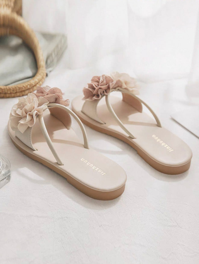 Pair of beige sandals with floral decorations on a white surface