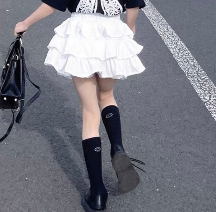 Person wearing a white skirt and black knee-high boots on a street.
