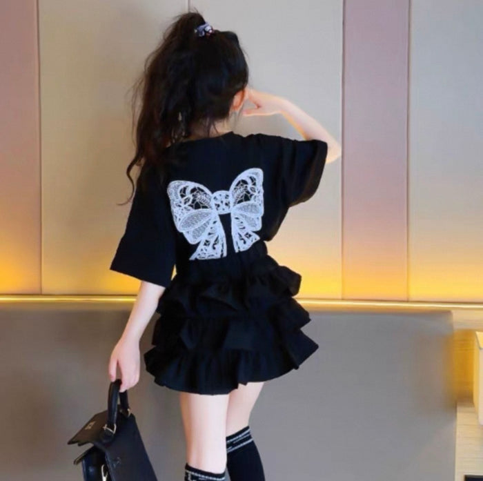 Person wearing a black outfit with a butterfly design, standing in an indoor setting.