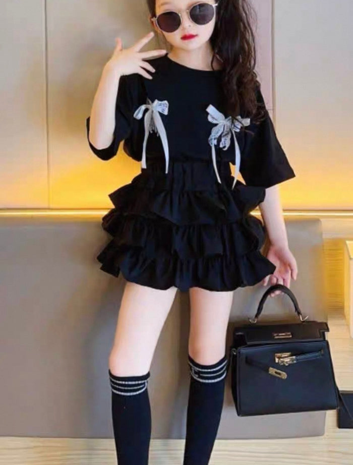Person wearing a black dress with ruffles and bows, holding a black handbag.
