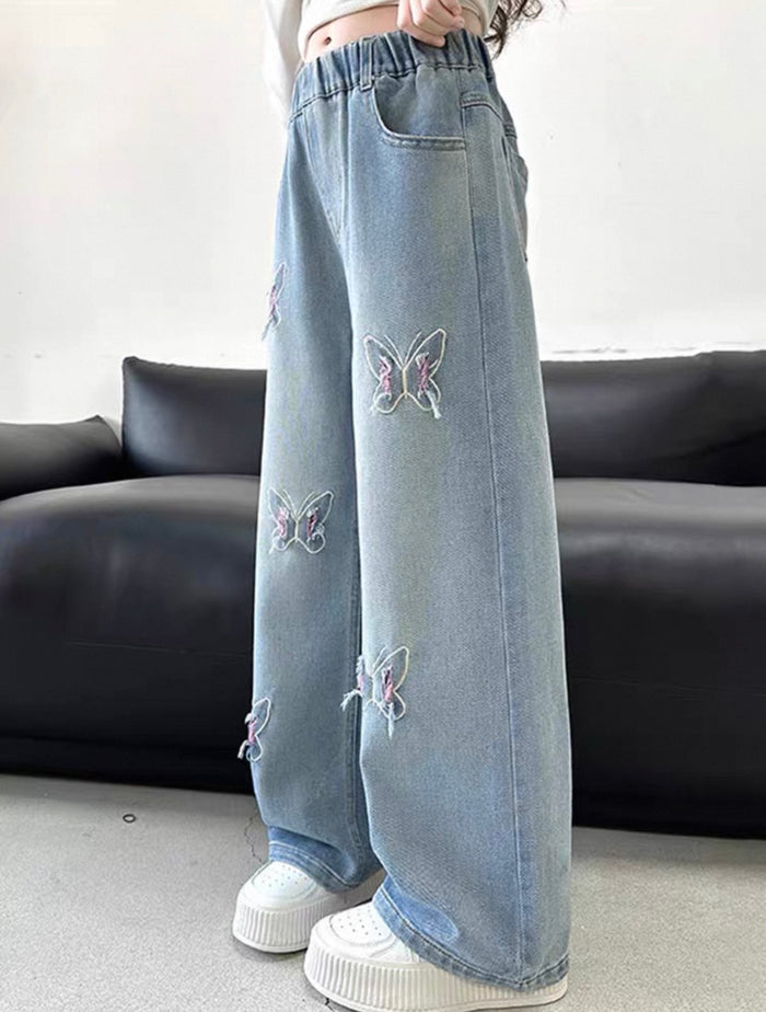Light blue jeans with butterfly embroidery worn by a person, sitting on a black couch.