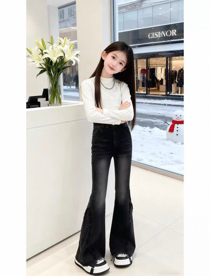 Person wearing a white long-sleeve top and black flared jeans standing in a store with a snowman decoration outside.