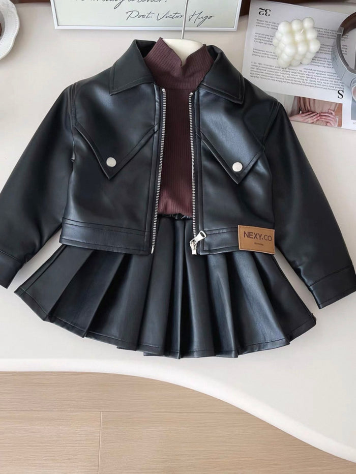 Black leather jacket and skirt set on a white surface with a magazine in the background.