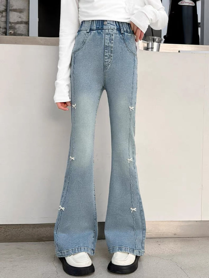 Person wearing light blue flared jeans with decorative elements indoors.