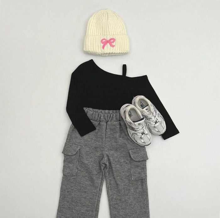 Black long-sleeve top, gray pants, white sneakers, and cream beanie with pink bow on a light gray background