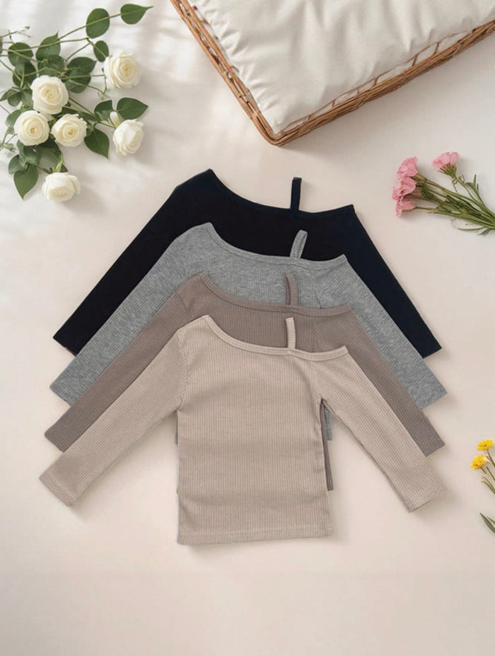 Four long-sleeve shirts in black, gray, and beige on a light surface with flowers around.