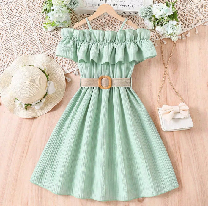 Mint green dress with ruffled top and belt, placed on a wooden surface with decorative items.