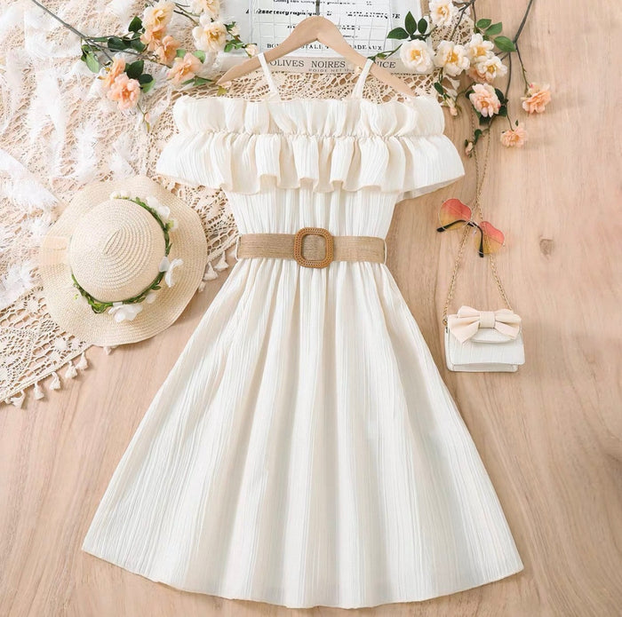 White dress with a belt, straw hat, and small handbag on a wooden surface with flowers.