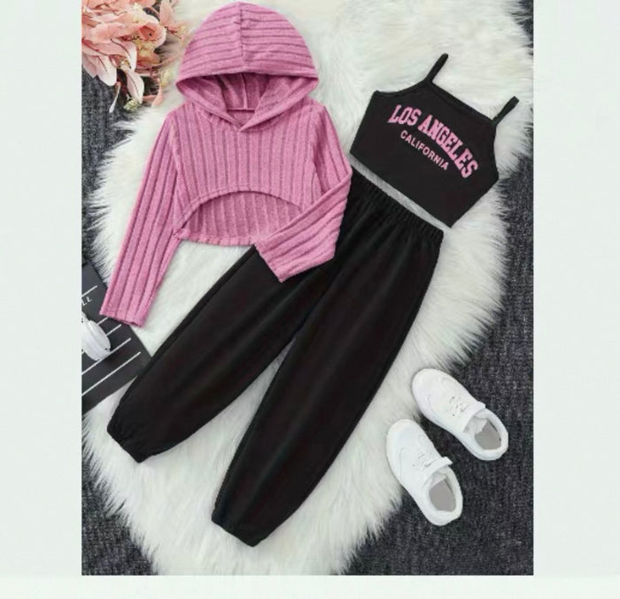 Pink hoodie, black tank top with 'Los Angeles California' text, black pants, and white sneakers on a textured surface.