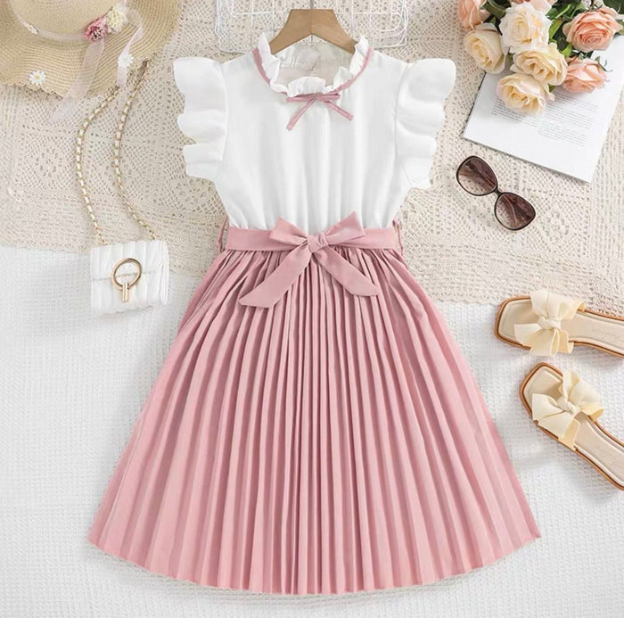 White blouse with pink pleated skirt on a textured surface with accessories.