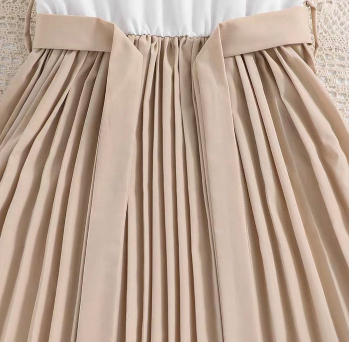 Close-up of a beige pleated skirt with a white top underneath.