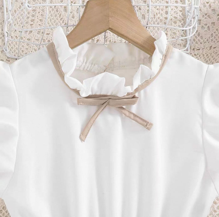 White blouse with ruffled collar and bow tie on a wooden hanger against a lace curtain background