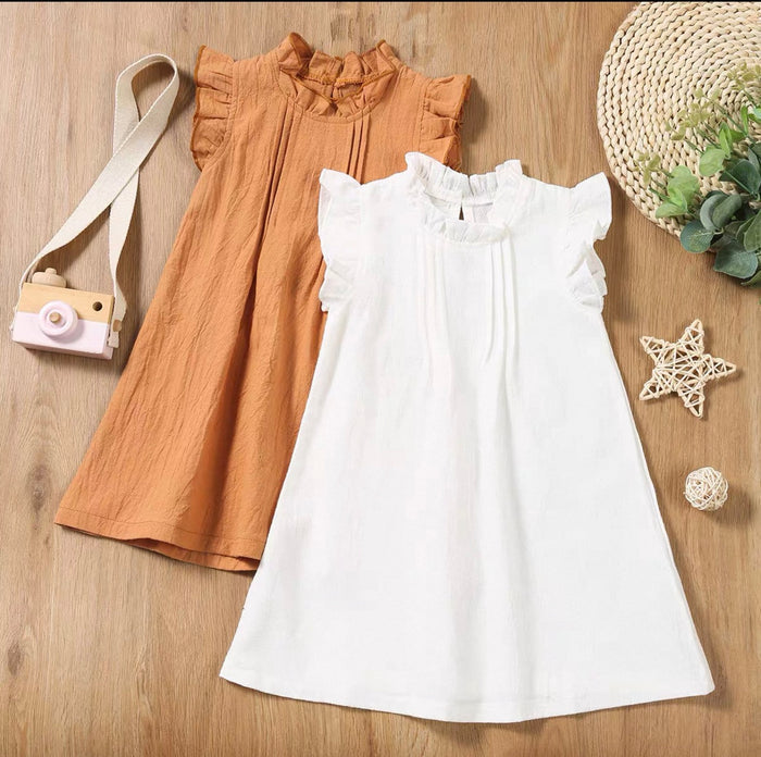 Two dresses, one brown and one white, on a wooden surface with decorative items.