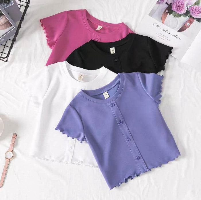 Four short-sleeve shirts in purple, black, and white on a white surface with a watch and magazine in the background.