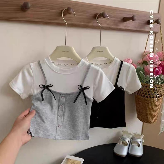Children's clothing set with a gray and black top and white shorts on hangers against a wooden rack.