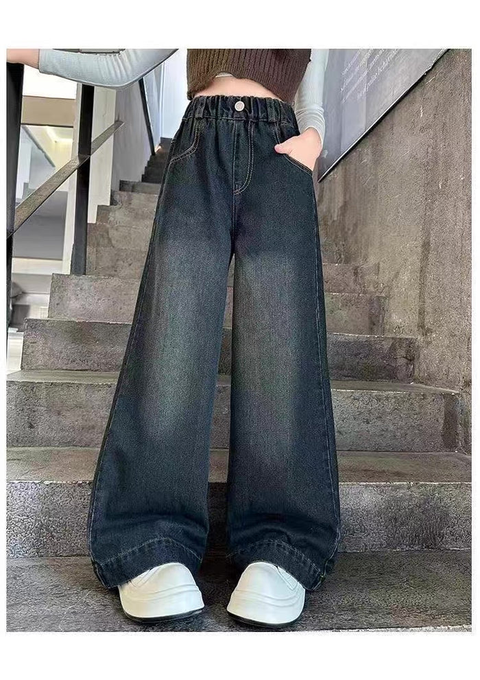 Person wearing wide-leg jeans and white sneakers on a staircase.