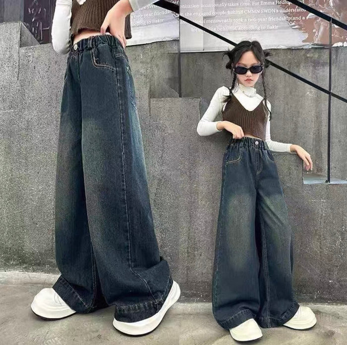 Two people wearing wide-leg jeans in front of a gray wall.