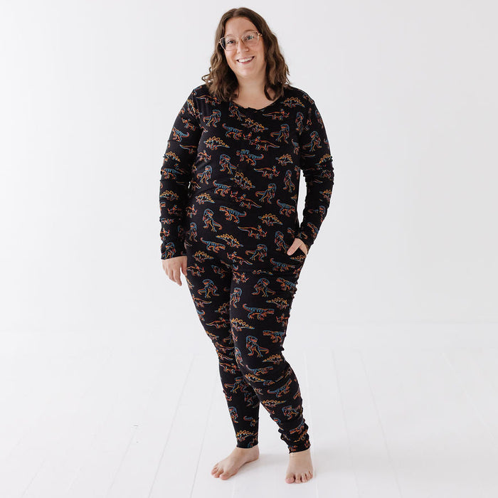 A woman wearing a matching black long-sleeve pajama top and pants set with an all-over orange and blue pattern, standing against a clean white studio background.