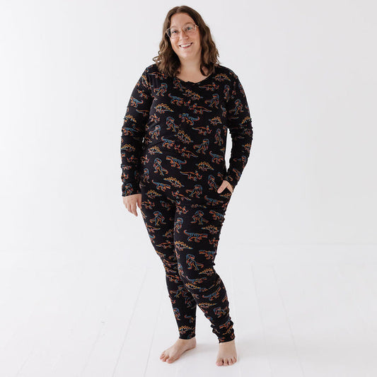 A woman wearing a matching black long-sleeve pajama top and pants set with an all-over orange and blue pattern, standing against a clean white studio background.
