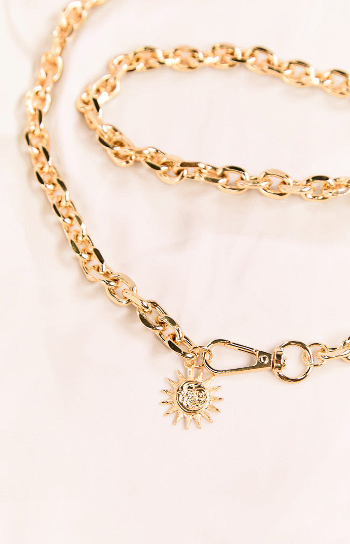 Detail shot of the gold chain belt's carabiner clip closure and a round sun charm with a face