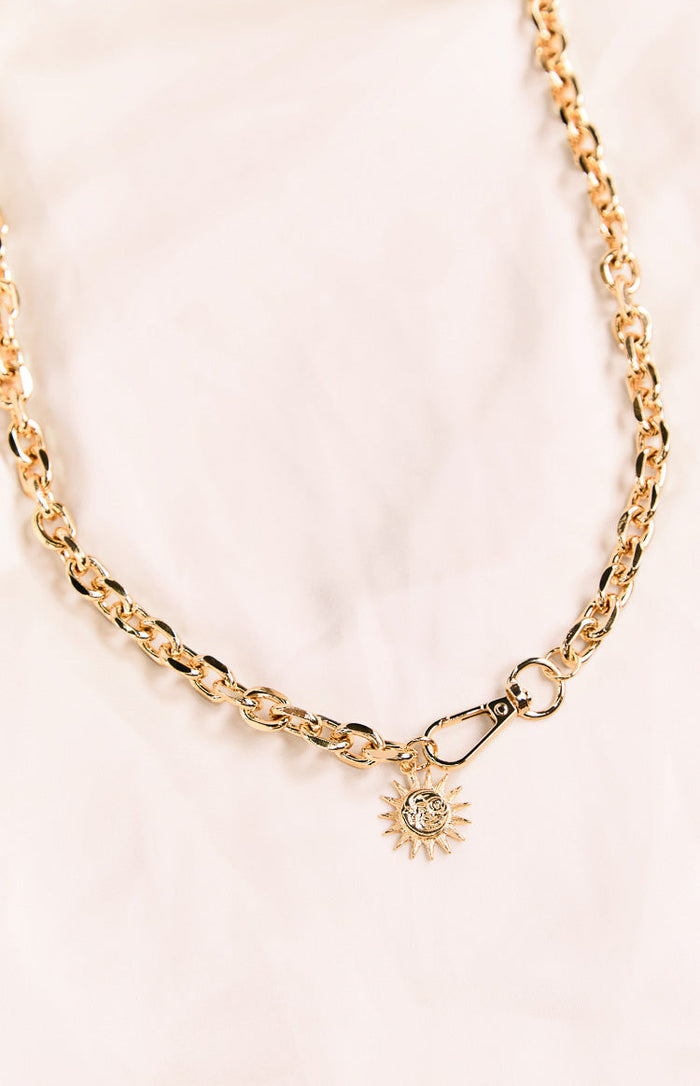 Close-up of the gold chain belt's carabiner clip and the detailed sun and moon charm
