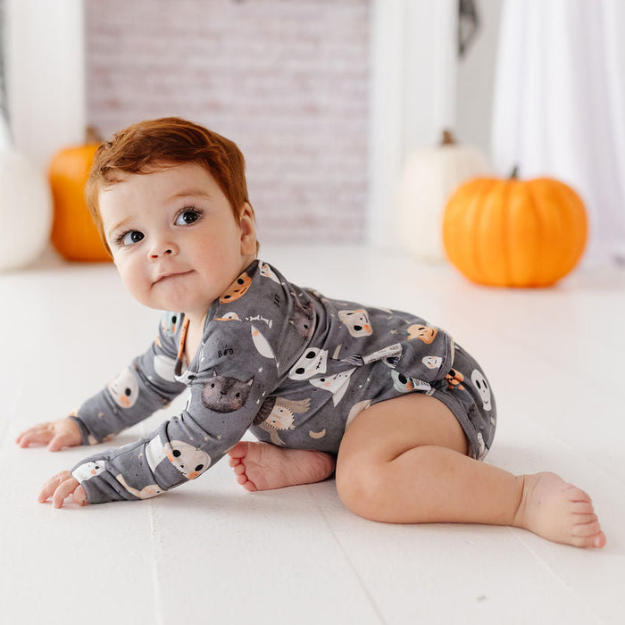 A baby wearing a gray long-sleeve romper with a fox print pattern, crawling on a white wooden floor in a decorated room with pumpkins and a ghost.