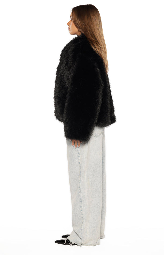 Side view of a black faux fur jacket showing its shaggy texture and cropped length