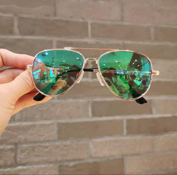 Aviator sunglasses with green reflective lenses held against a brick wall.