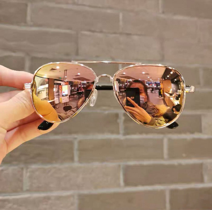 Gold reflective sunglasses held in front of a brick wall