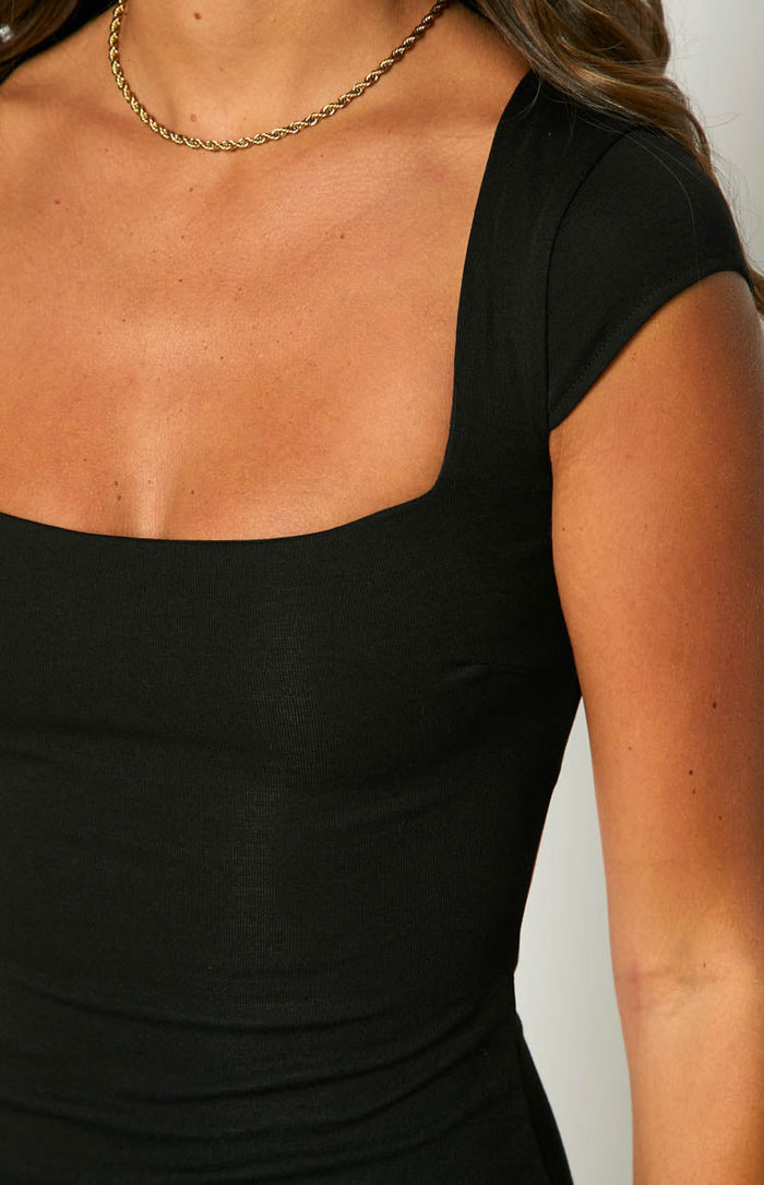 Close-up of the square neckline and short cap sleeves of a black ribbed mini dress