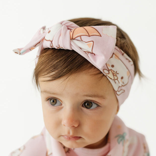 A baby wearing a light pink patterned headband and matching short-sleeve top against a plain white background.
