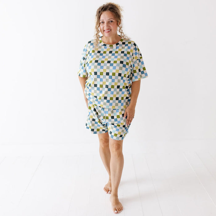 A woman modeling a matching two-piece lounge set consisting of a short-sleeve top and shorts, featuring a geometric checkered pattern in light blue, yellow, and dark green on a white background.