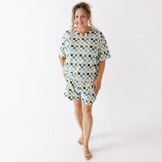 A woman modeling a matching two-piece lounge set consisting of a short-sleeve top and shorts, featuring a geometric checkered pattern in light blue, yellow, and dark green on a white background.