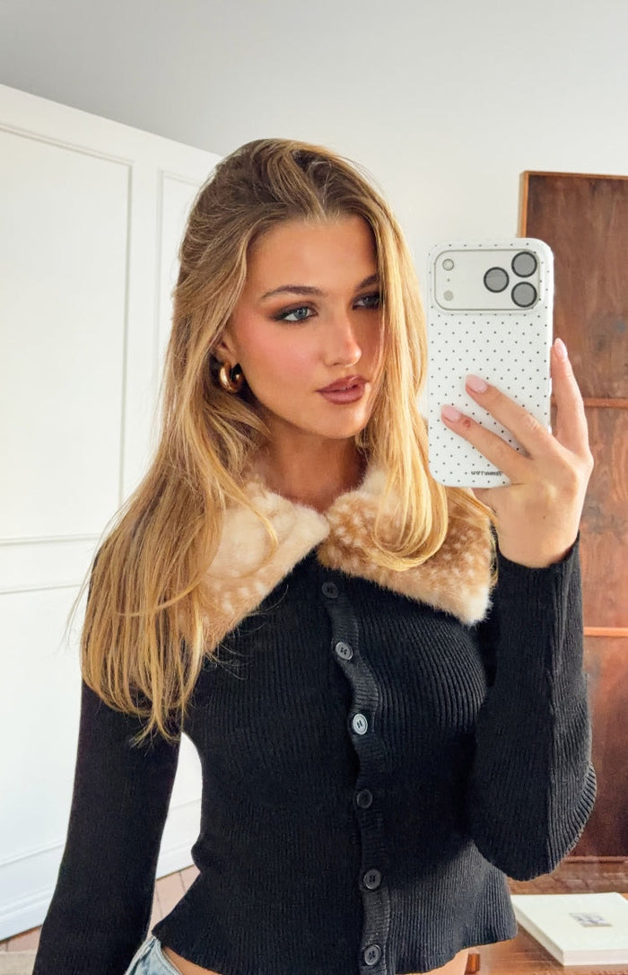 Close-up of a black ribbed knit cardigan with a light brown speckled fur trim collar and front buttons