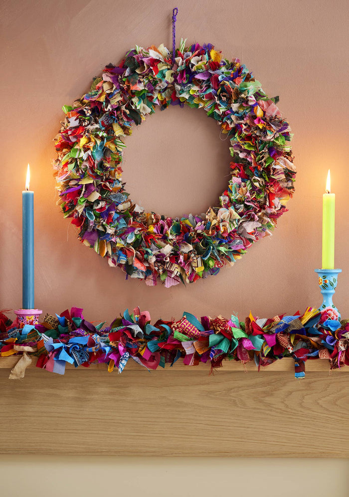 Colorful fabric wreath and garland on a fireplace mantle with candles.