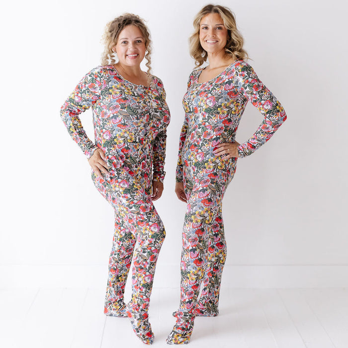 Two women modeling matching long-sleeve jumpsuits with a colorful floral print, standing against a plain white studio background.