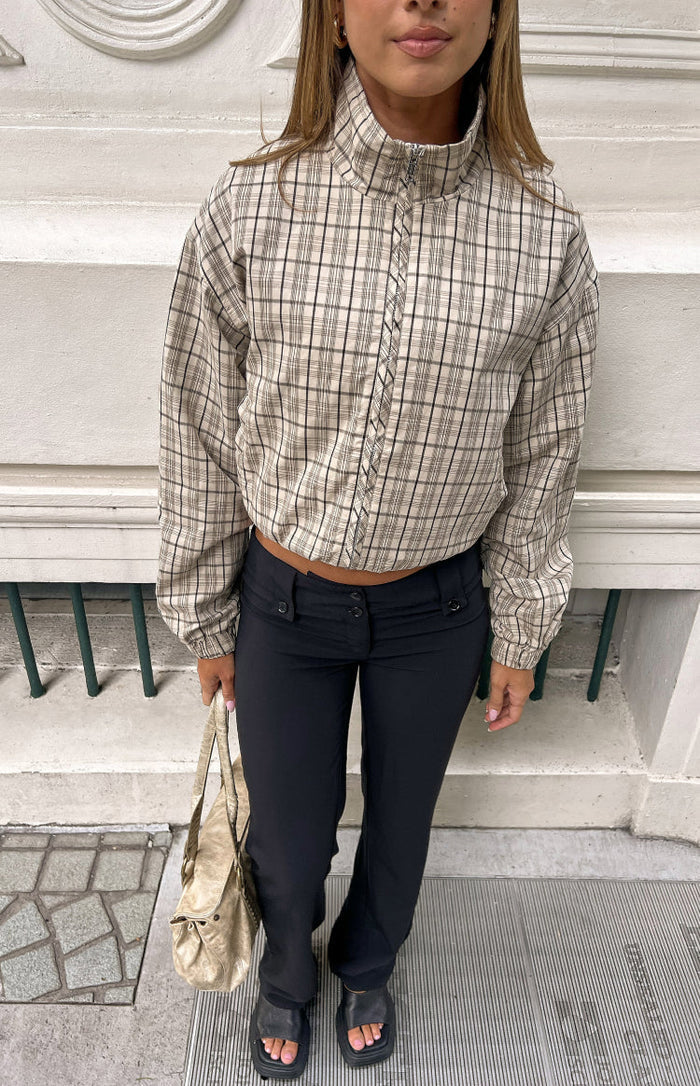 Front view of a beige plaid funnel neck jacket with a full zip, elasticated cuffs, and cropped blouson hem