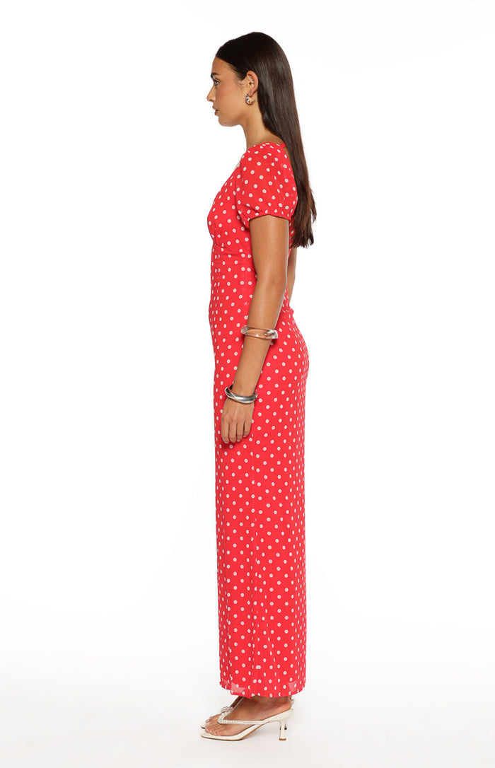 Side view of a red maxi dress with white polka dots, short sleeves, a fitted waist, and a flowing skirt