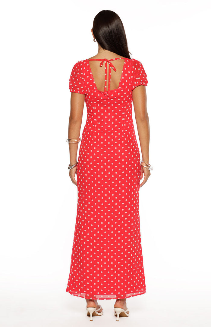 Back view of a red polka dot maxi dress with a square neckline, tie detail, and short puff sleeves