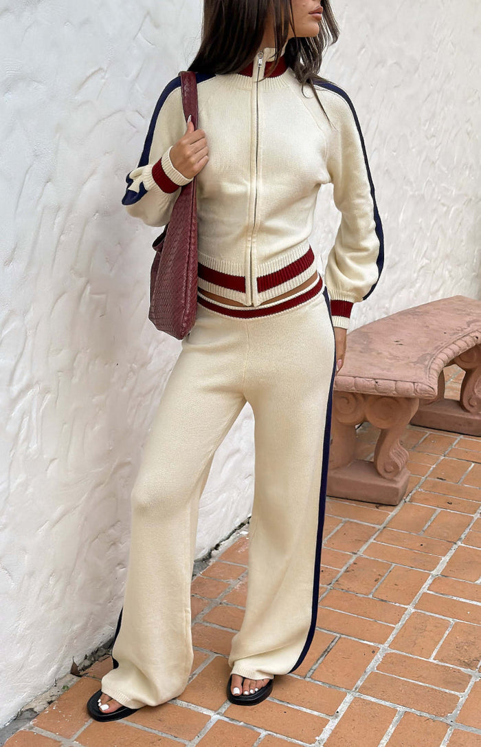 Cream knit wide-leg track pants with dark blue side stripes and ribbed red and cream waistband
