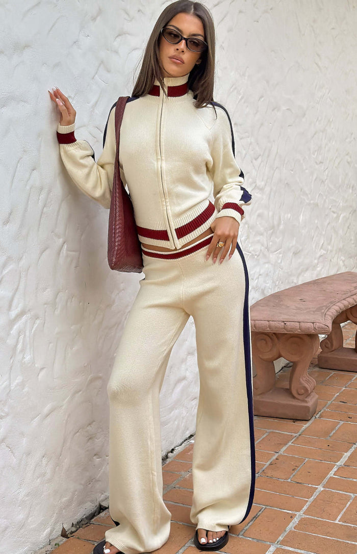 Cream knit jacquard track pants with a wide-leg fit, dark blue side stripes, and a red and cream striped waistband