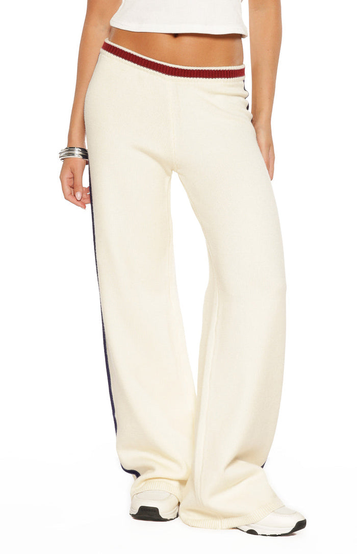 Close-up of cream knit track pants with a red and white ribbed waistband and dark blue side stripe