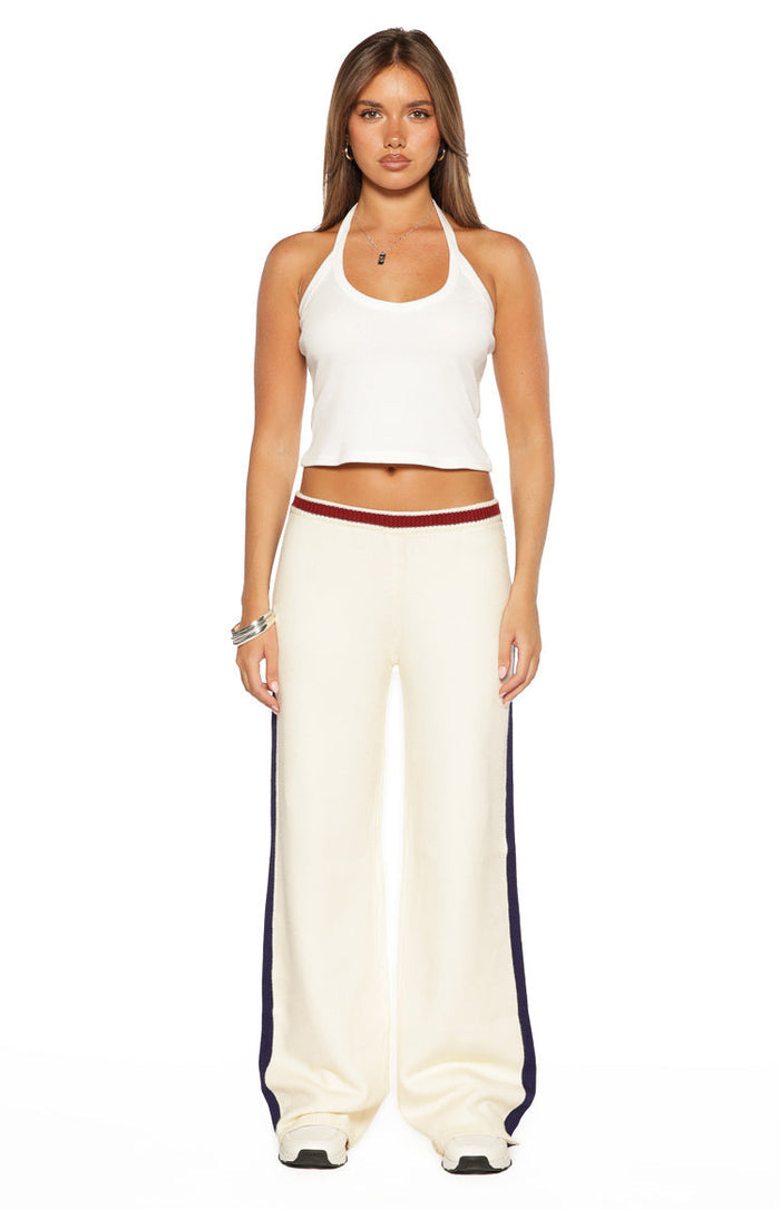 Cream knit wide-leg track pants featuring a red and white striped ribbed waistband and navy side stripes